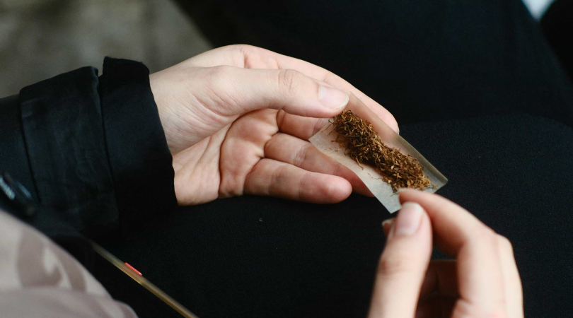 Two hands holding a rolling paper while rolling a joint. 