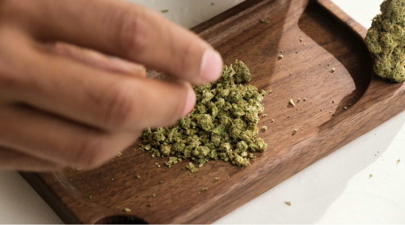 Hand putting ground THCa flower on a wooden tray.